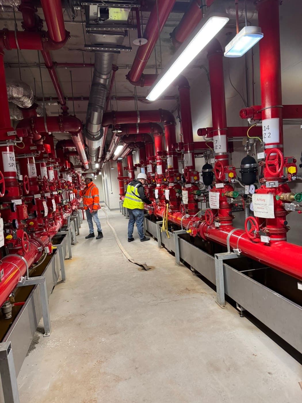 Zwei Monteure in Warnkleidung bei der Druckprobe an einer Ventilstation der Sprinkleranlage
