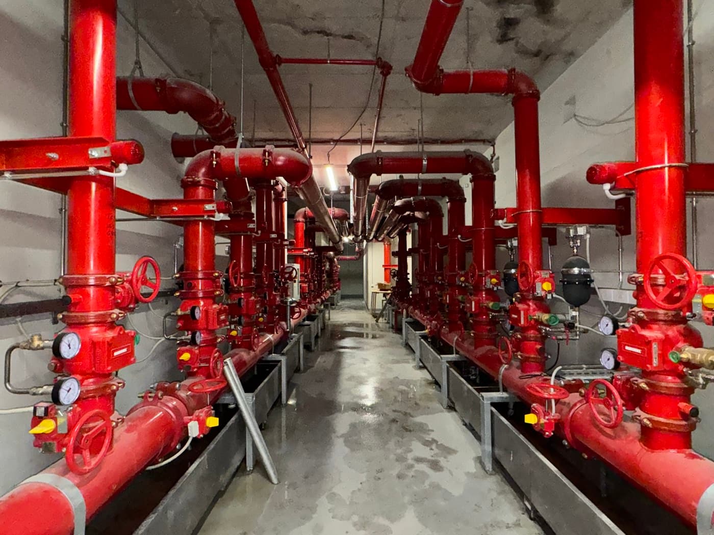 Sprinklerzentrale mit rot lackierten Steigleitungen, Ventilstationen und Manometern im Untergeschoss